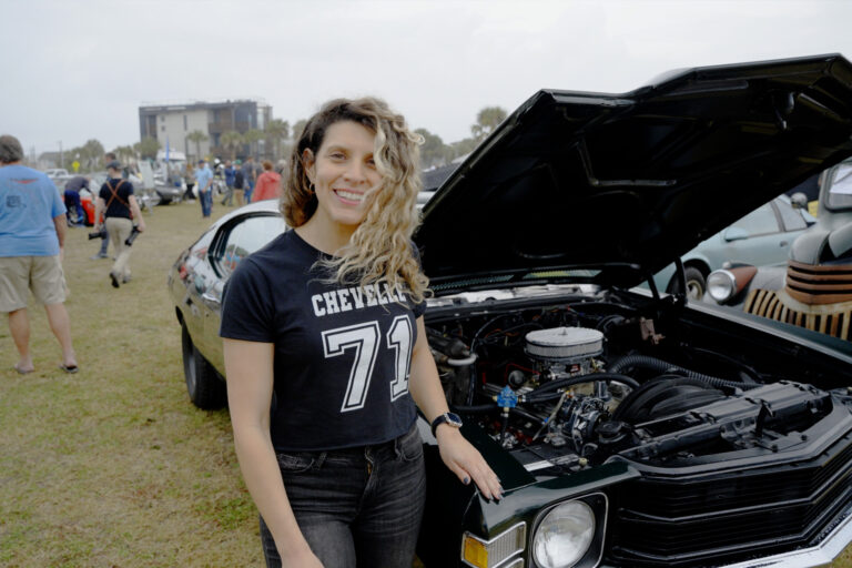 A person stands beside a black classic car with its hood raised at the Amelia Island Concours d’Lemons.