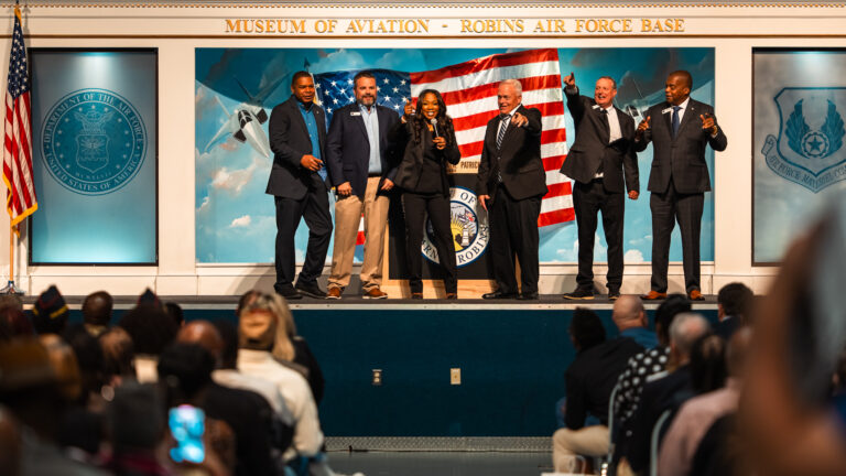 A group poses on stage beneath the Museum of Aviation sign at the Warner Robins State of the City Address.