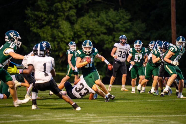 Football players in green and white uniforms converge around the ball carrier during Westfield versus Southland.