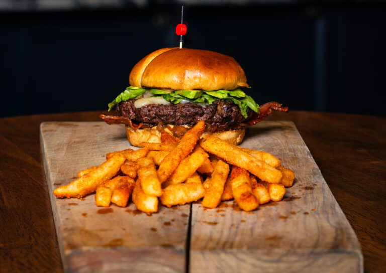 Burger with lettuce on a glossy bun, served with fries on a wooden board.