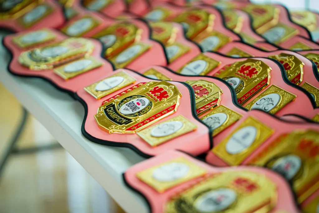 Multiple pink and gold championship boxing belts arranged on a table