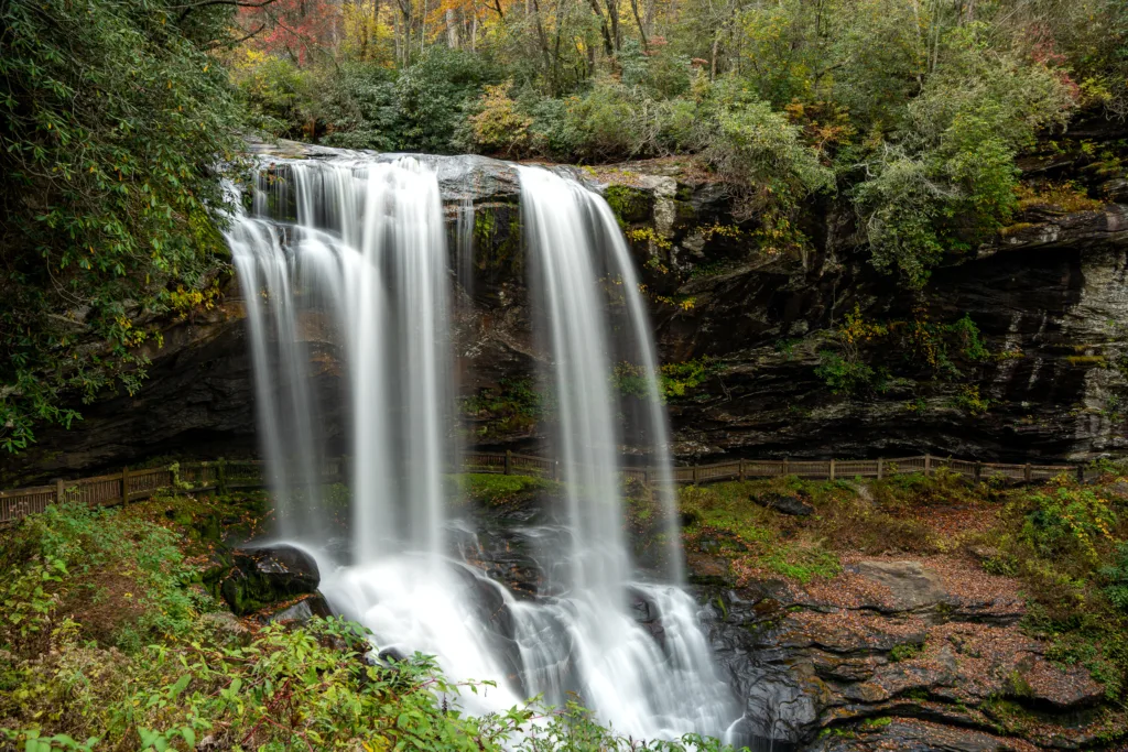 Long exposure of Dry Falls waterfall surrounded by autumn foliage in Highlands, North Carolina