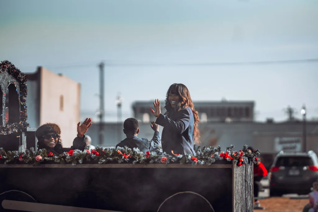 People wave from a festively decorated parade float on a city street
