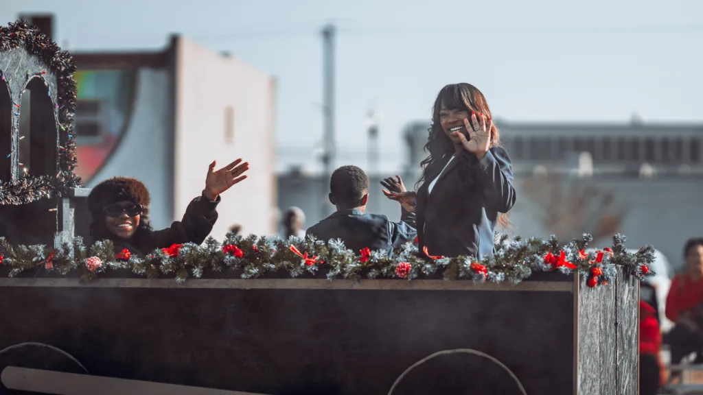 Smiling people waving from a flower garland holiday parade float
