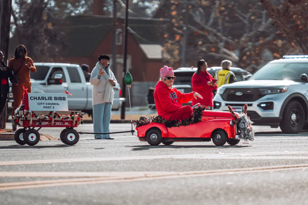 Person in red outfit driving small red car in holiday parade