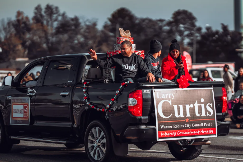 Black pickup truck decorated for a holiday parade with people riding in the back