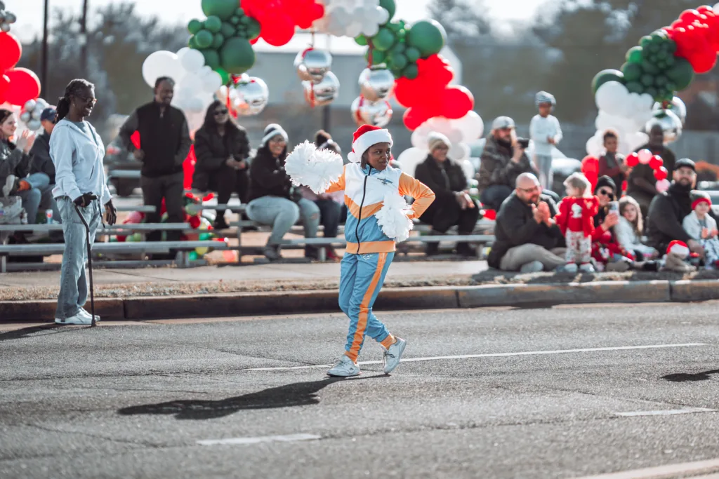 Young child in Santa hat marching with pom-poms in holiday parade