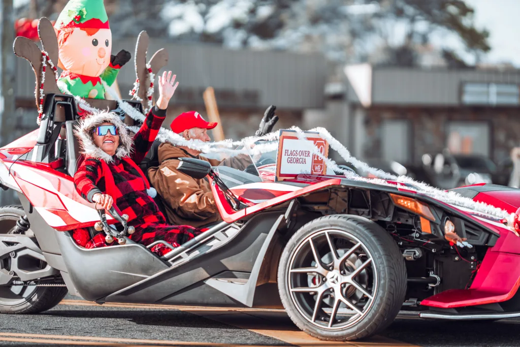 Smiling person in red plaid outfit waving from decorated three wheel car