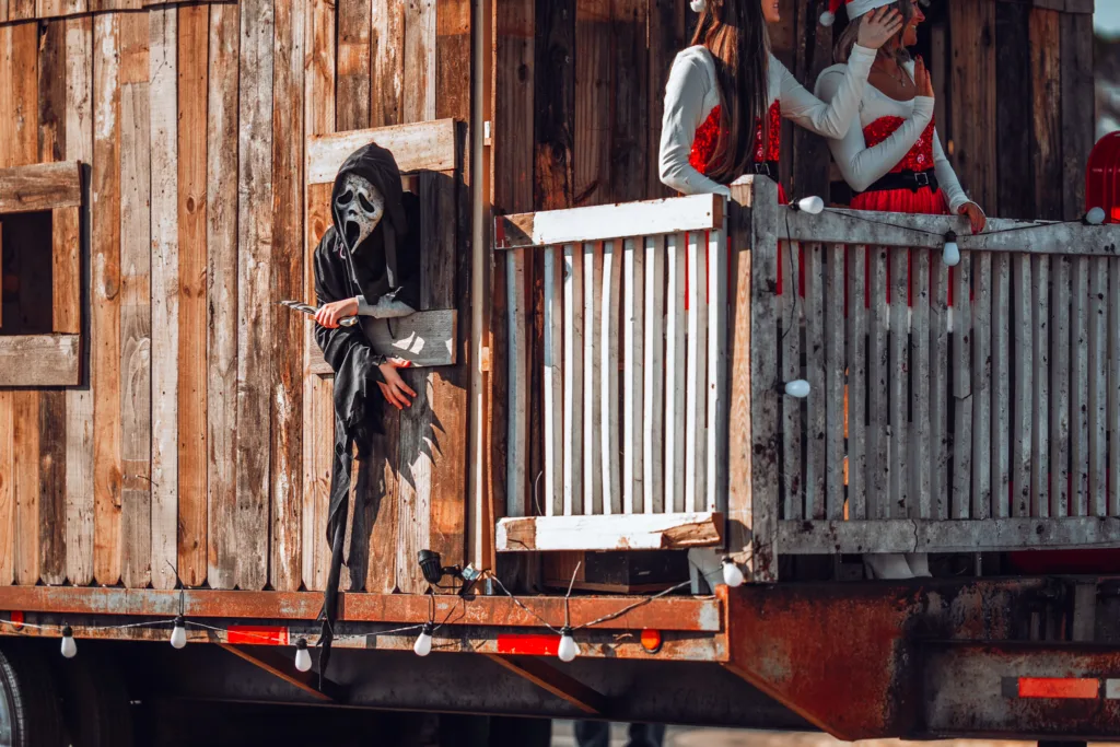 Masked figure in black robe peeking from rustic wooden parade float