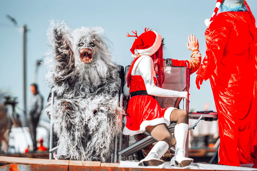 Person in furry monster costume beside Santa outfit on holiday parade float