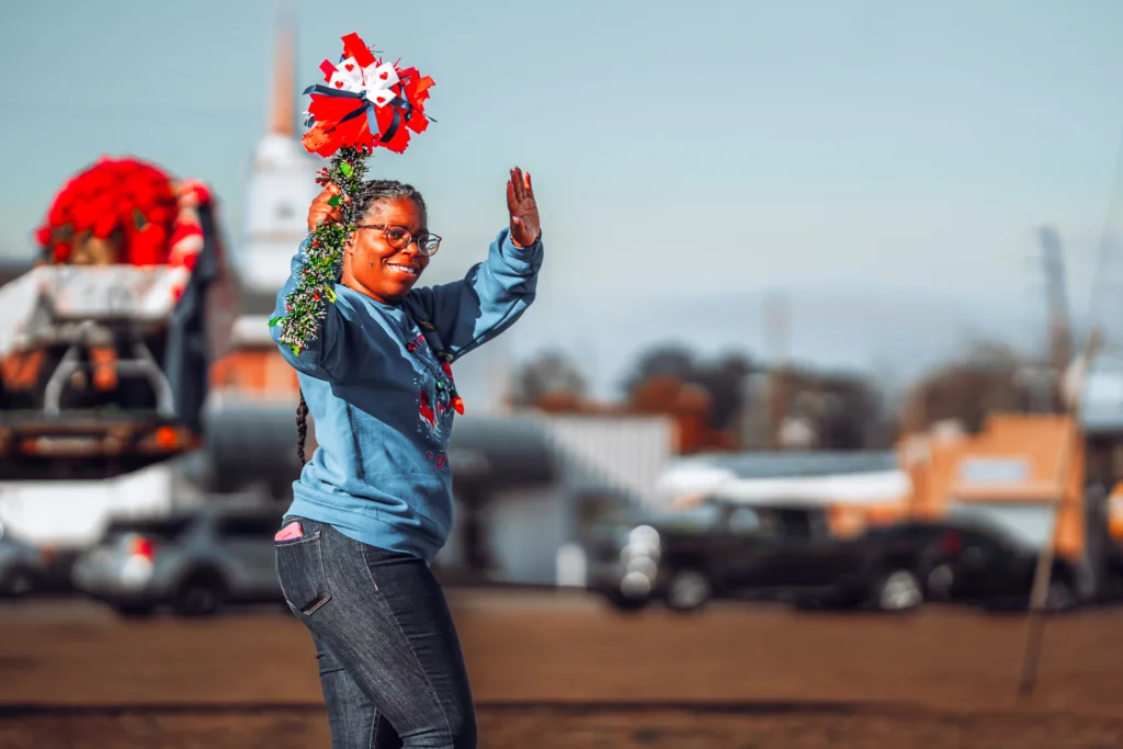 Smiling person in sweatshirt waving and holding red pom-poms at parade