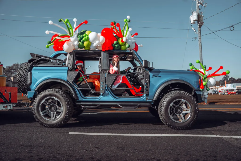 Blue Jeep covered in red, green and white balloons driving in a parade