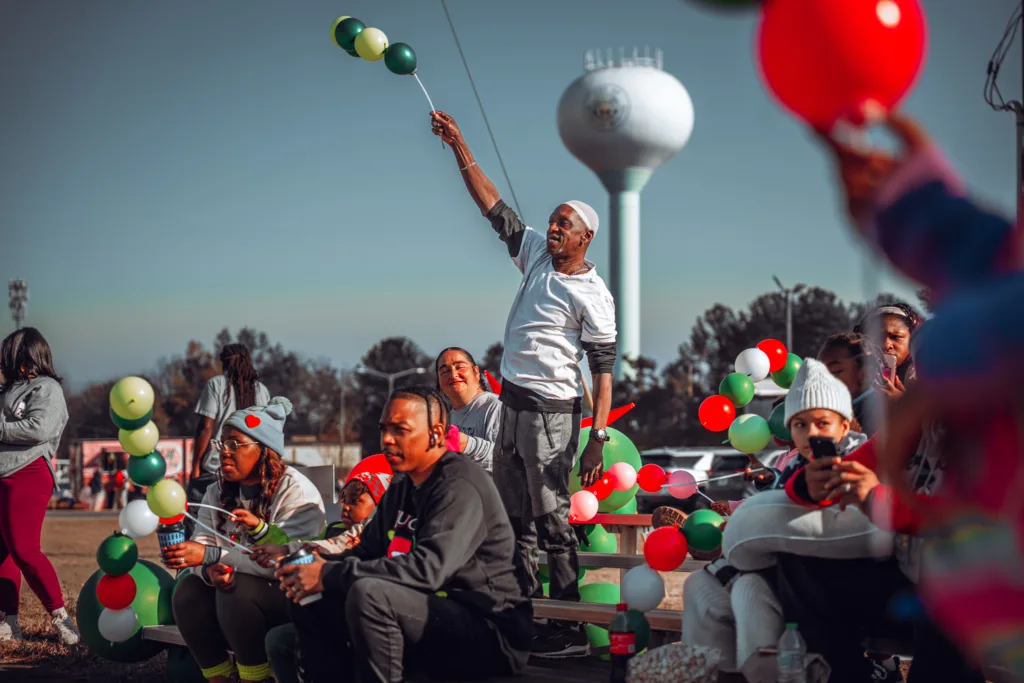 People sitting and standing at a parade holding red, green, and white balloons