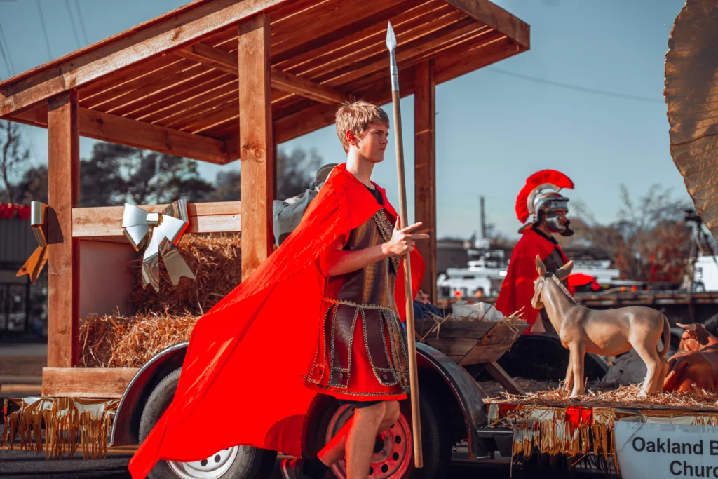Person in Roman soldier costume walking beside decorated parade float