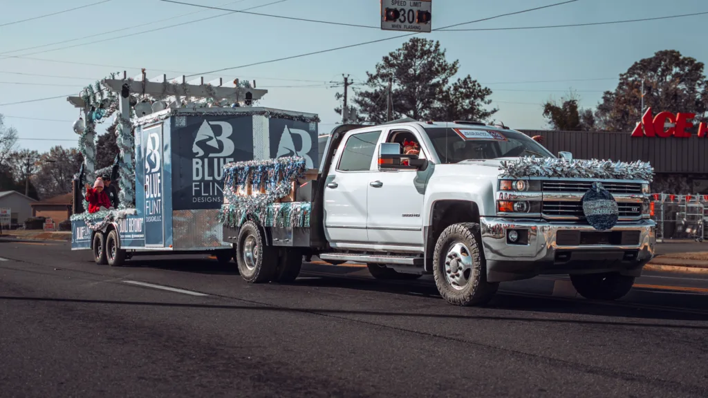 White pickup truck towing a decorated holiday parade float down a street