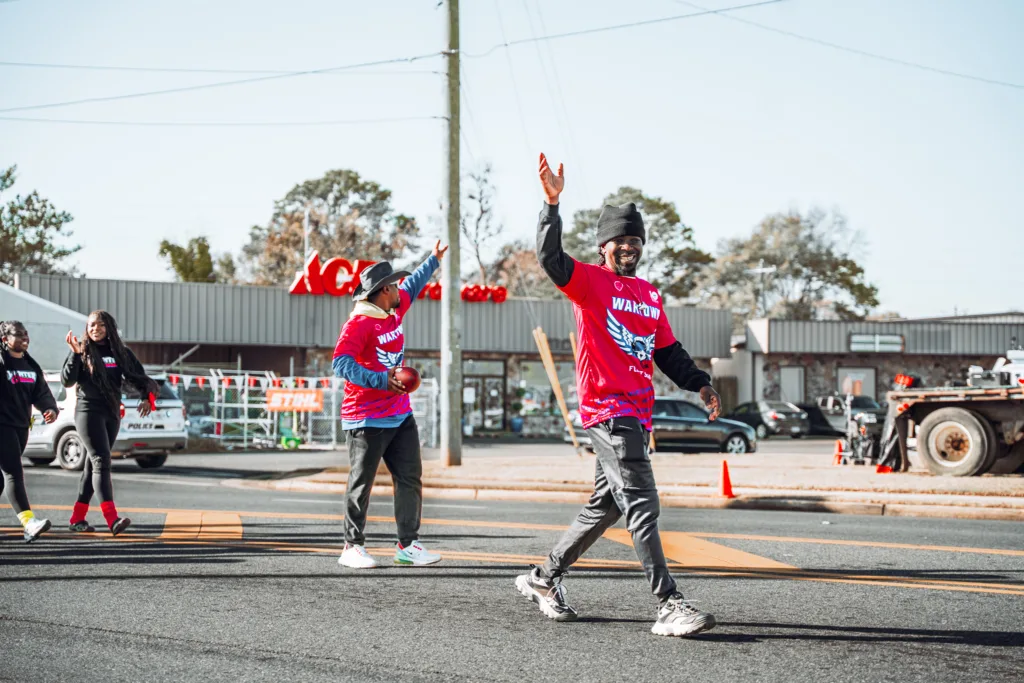 Parade walkers in matching shirts waving as they cross a city street