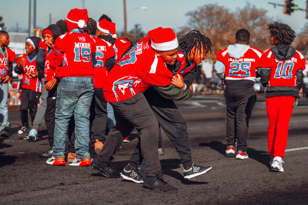 Youth football players in red jerseys and Santa hats playing in the street