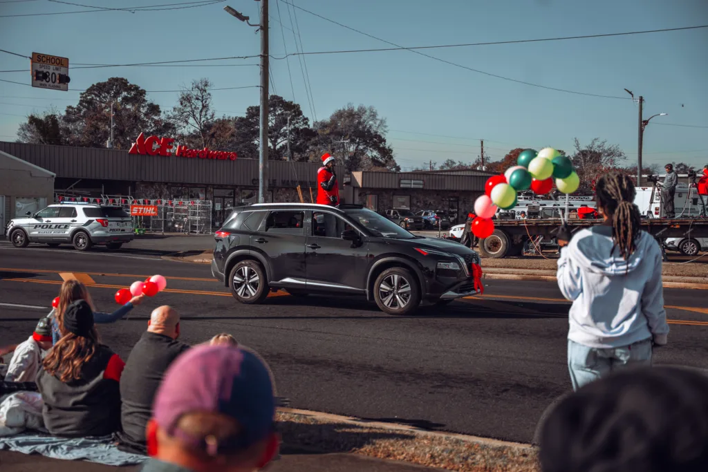 SUV decorated with balloons driving in a holiday parade past seated spectators