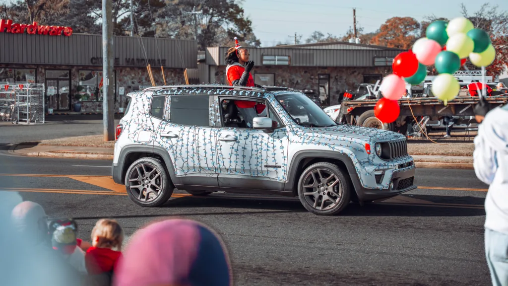 Decorated SUV drives in a holiday parade past spectators and balloons
