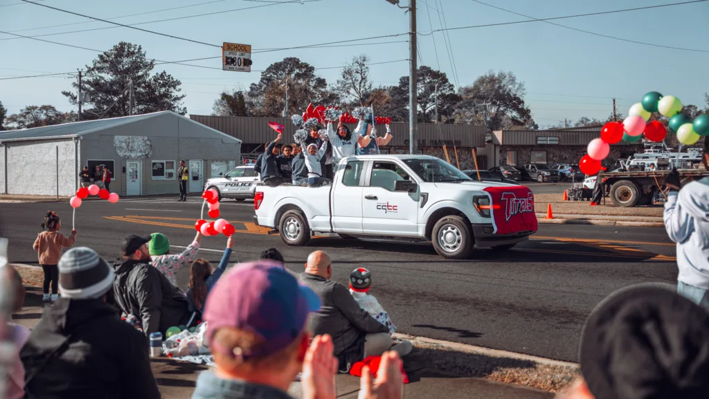 White pickup truck decorated with balloons drives past crowd at parade