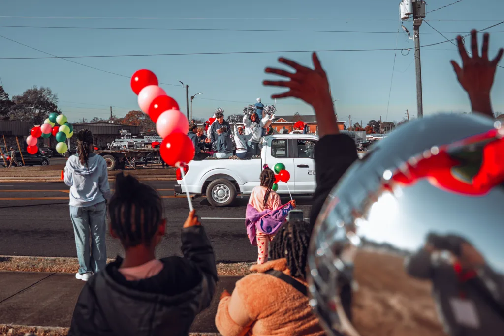 Crowd with balloons watching a festive parade and white pickup truck
