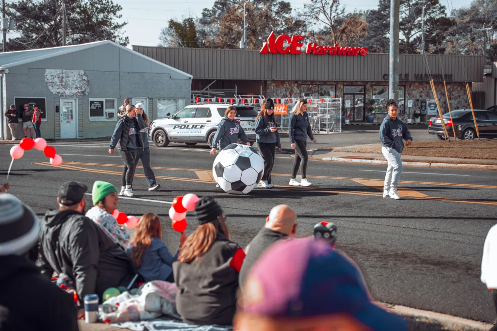 Parade performers roll a giant soccer ball past spectators on a street