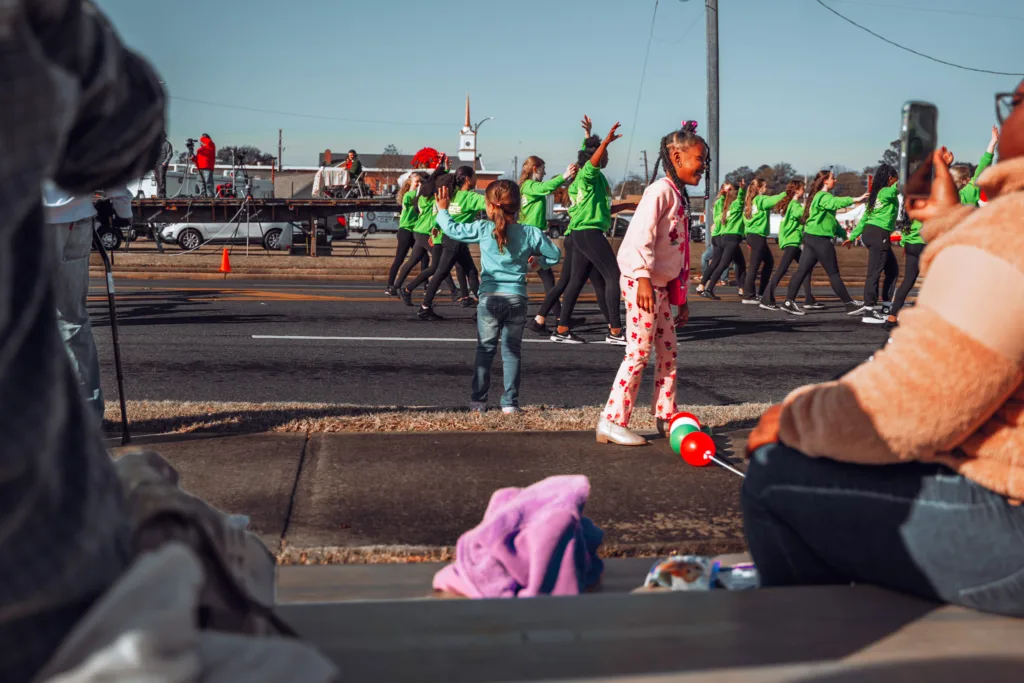 Children watch a group of dancers in green shirts perform in a street parade