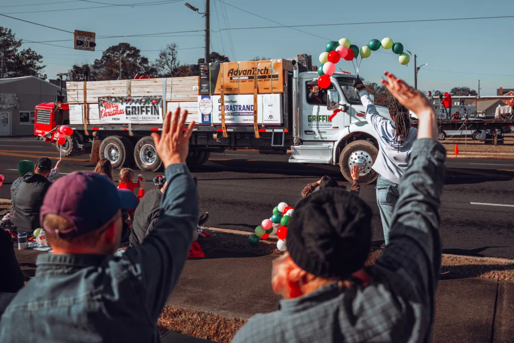 Parade spectators wave at a decorated flatbed truck with balloons