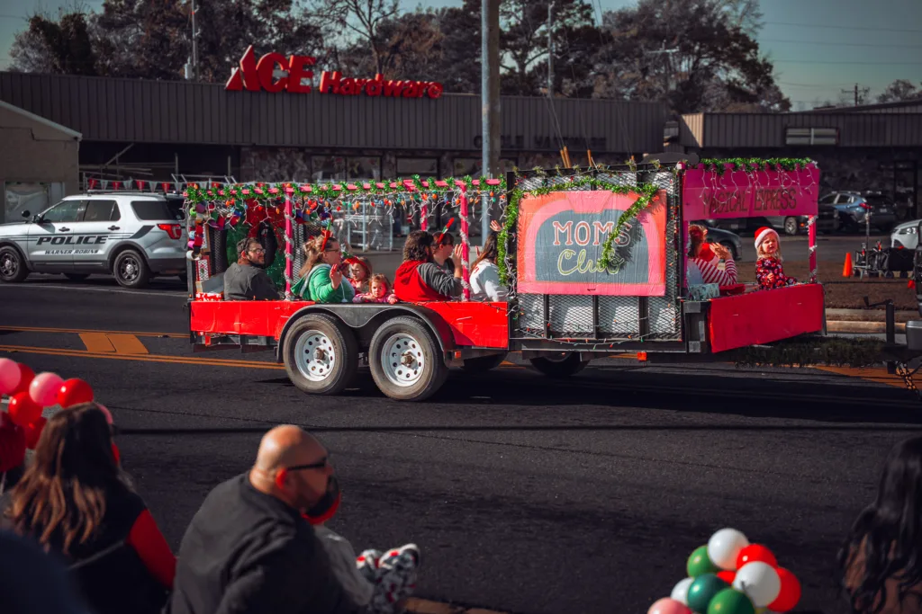 Children riding on a festive holiday parade float labeled Mom’s Club