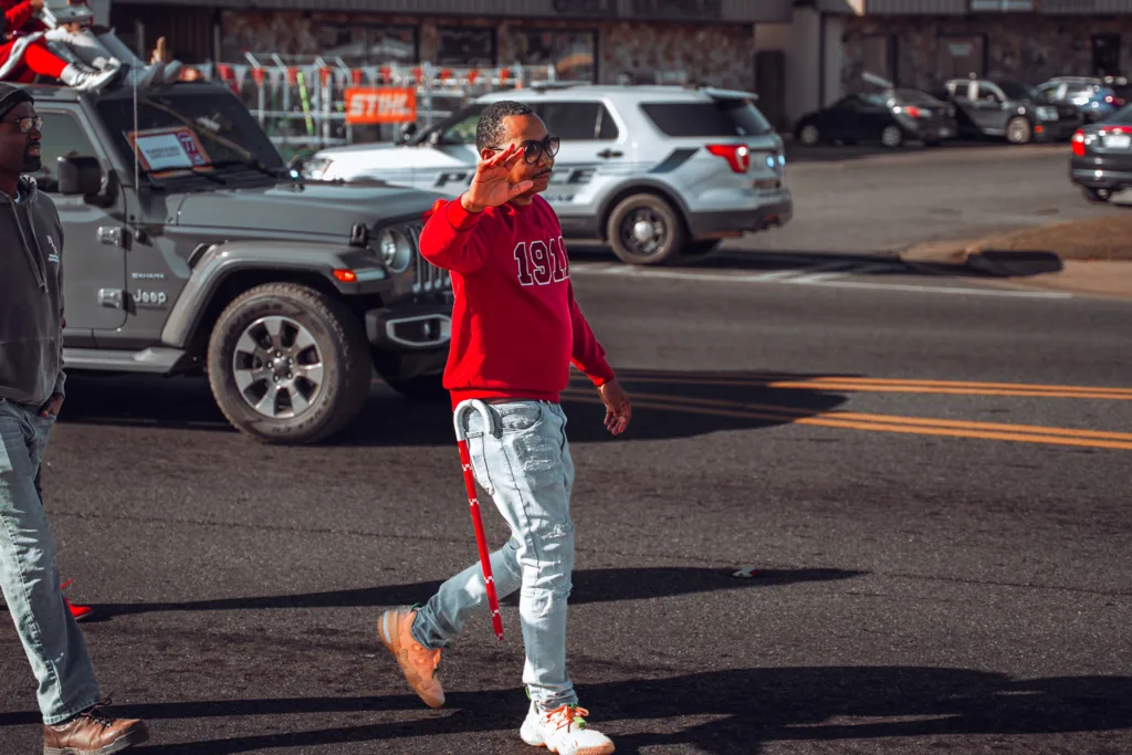 Man in red 1931 sweatshirt walking along street during parade