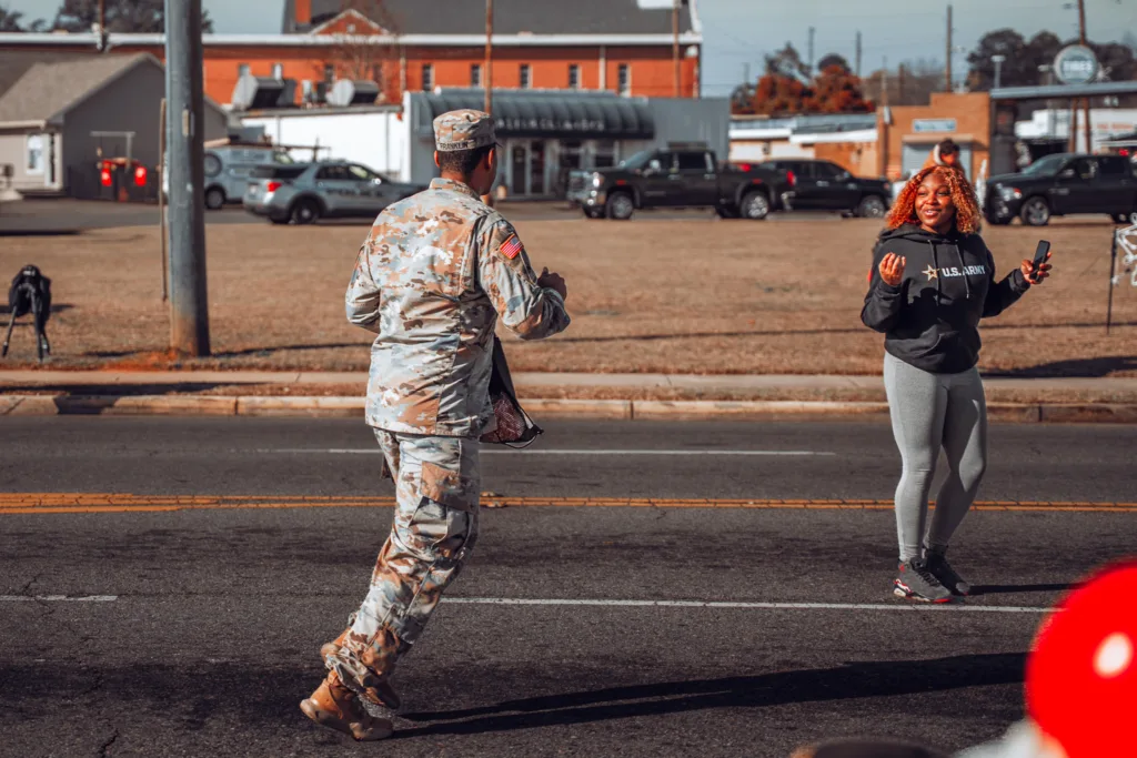 Uniformed soldier walking toward smiling woman on roadside during parade