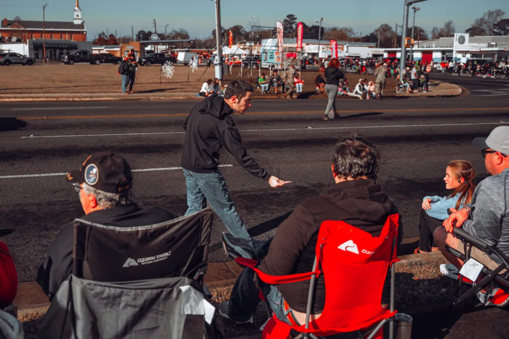 Man handing out items to parade spectators seated along a street