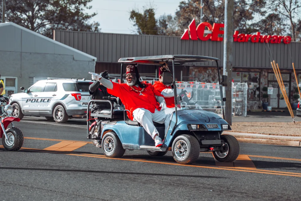 Shriners in red jackets riding a golf cart during a street parade