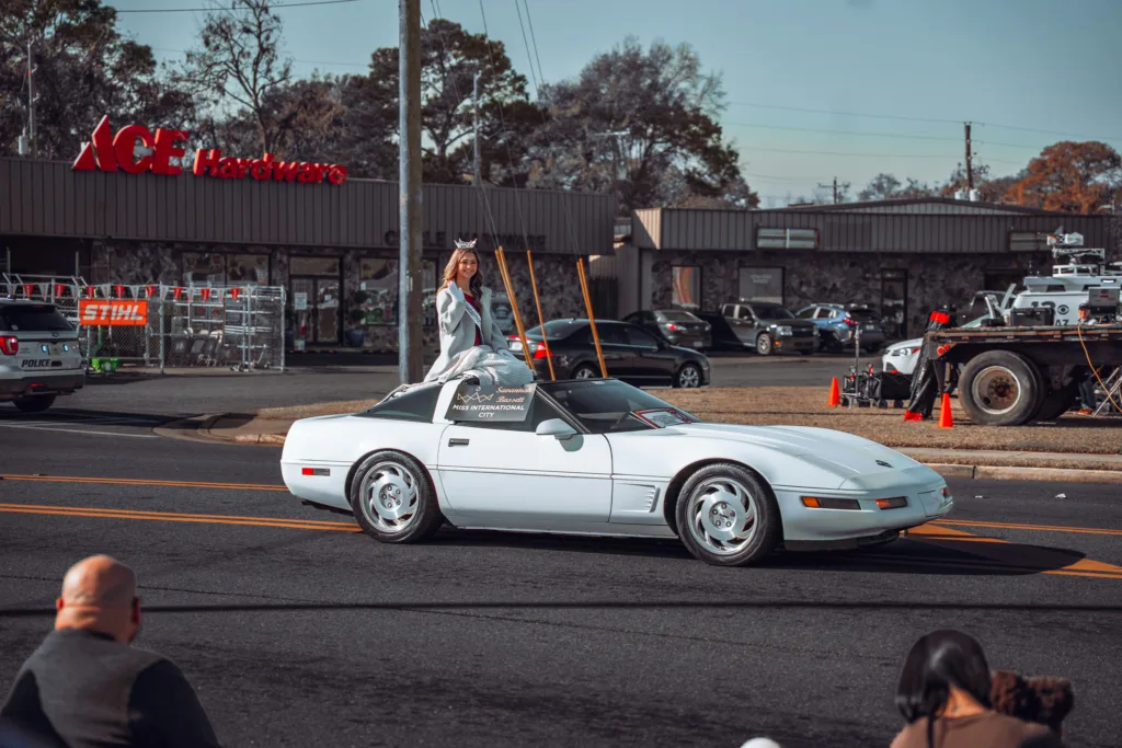 Parade queen standing in white convertible Corvette on city street
