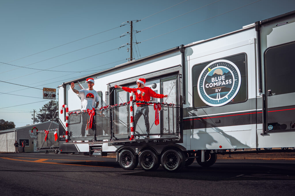 Blue Compass RV trailer with people in Santa hats on festive balcony
