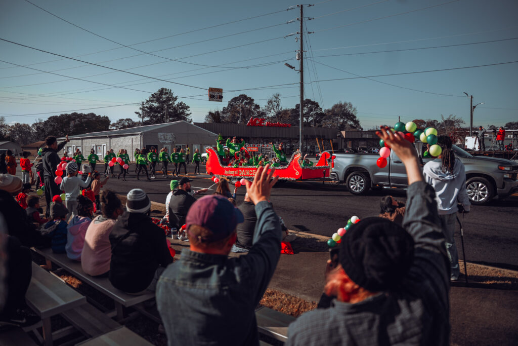 Crowd watching a red Christmas parade float with performers in green costumes