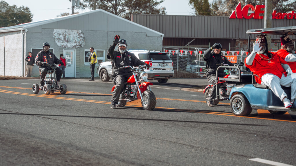 Parade participants riding mini bikes and a golf cart down a city street