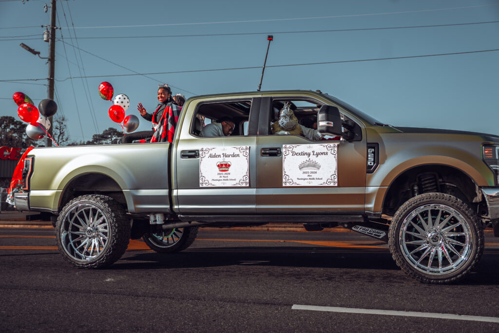 Lifted pickup truck with parade signs and balloons driving down street