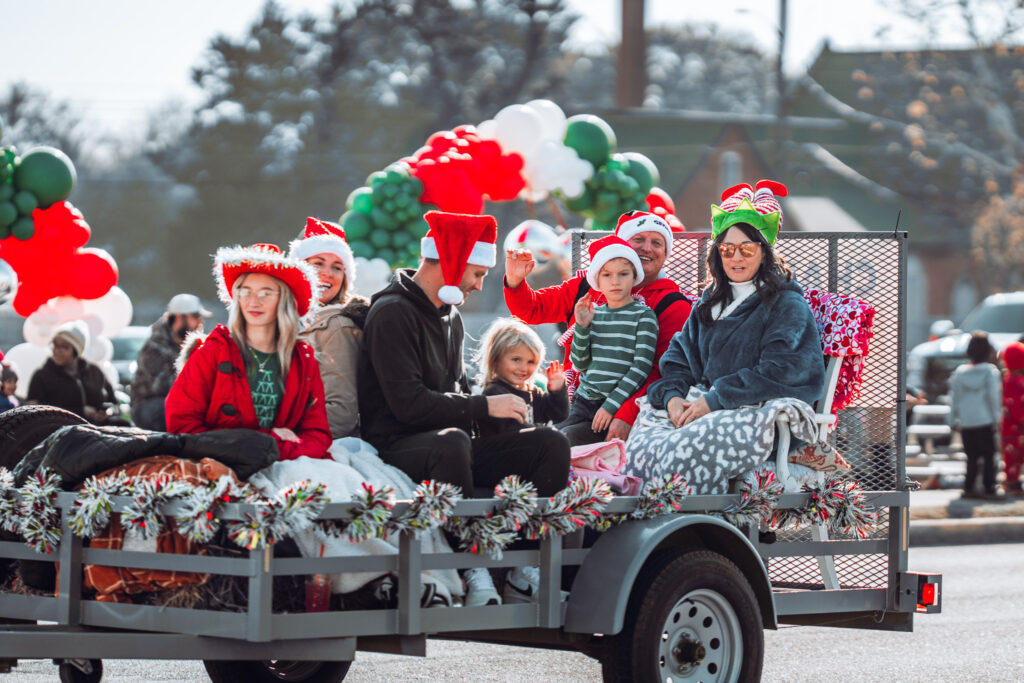 Group of people in Santa hats riding a decorated trailer in a Christmas parade