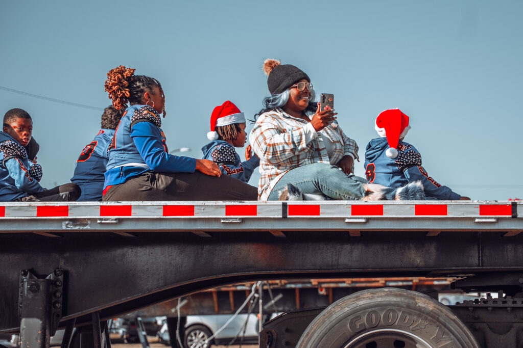 Adults and children sit on a flatbed trailer during a holiday parade