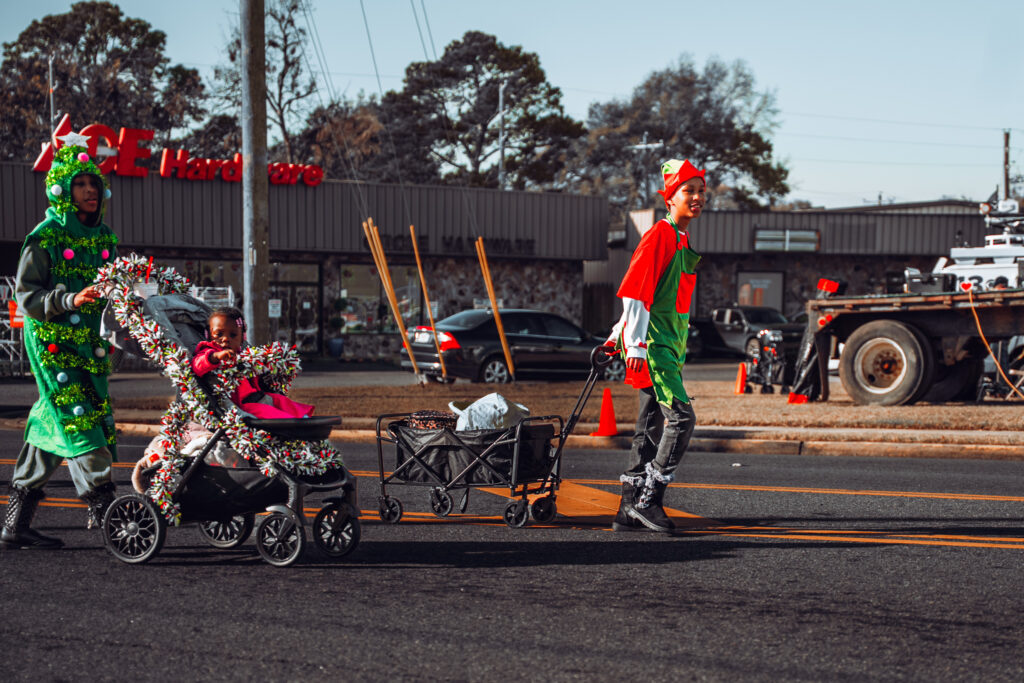 Adults in Christmas costumes pushing stroller and wagon in street parade