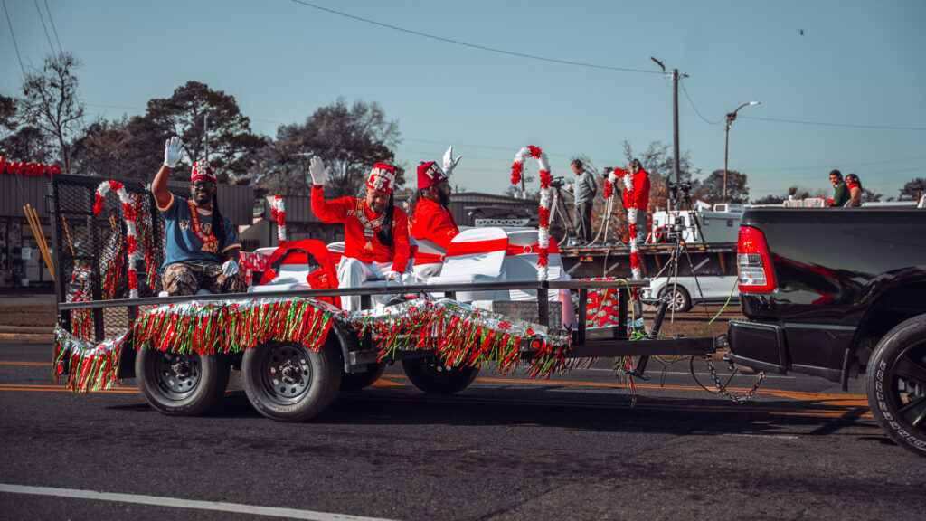 People in red costumes waving from a decorated holiday parade float