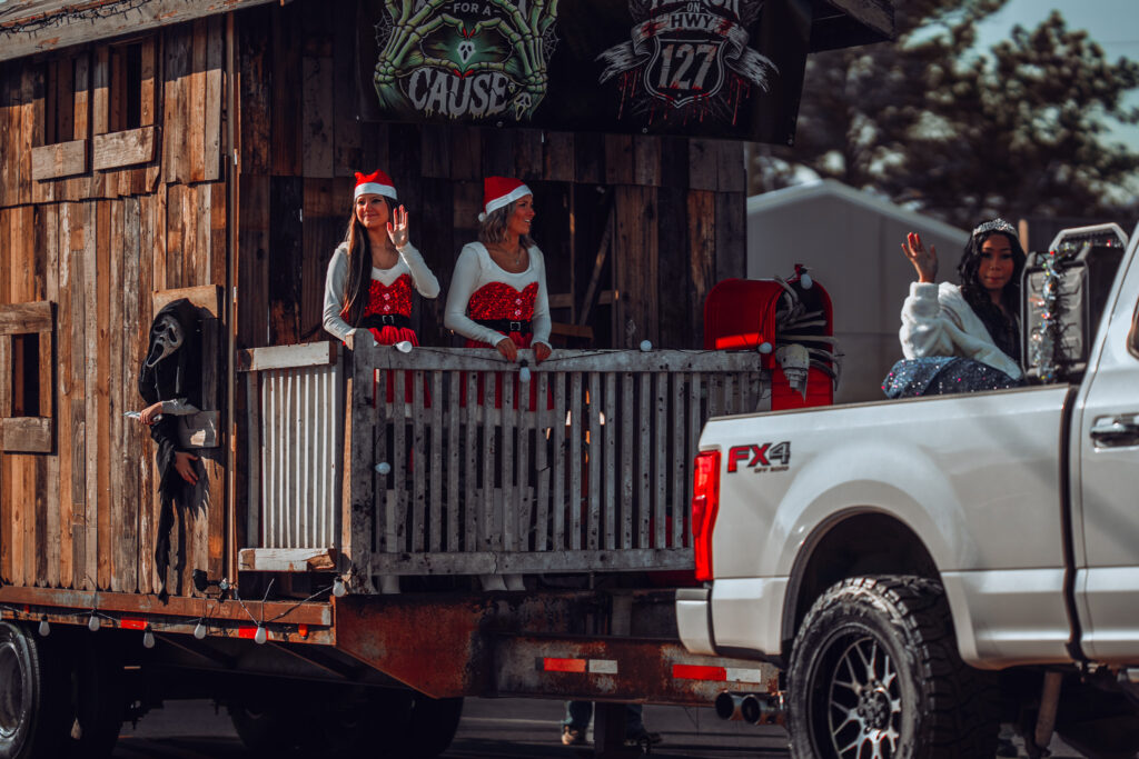 Women in Santa hats on rustic cabin parade float pulled by pickup truck