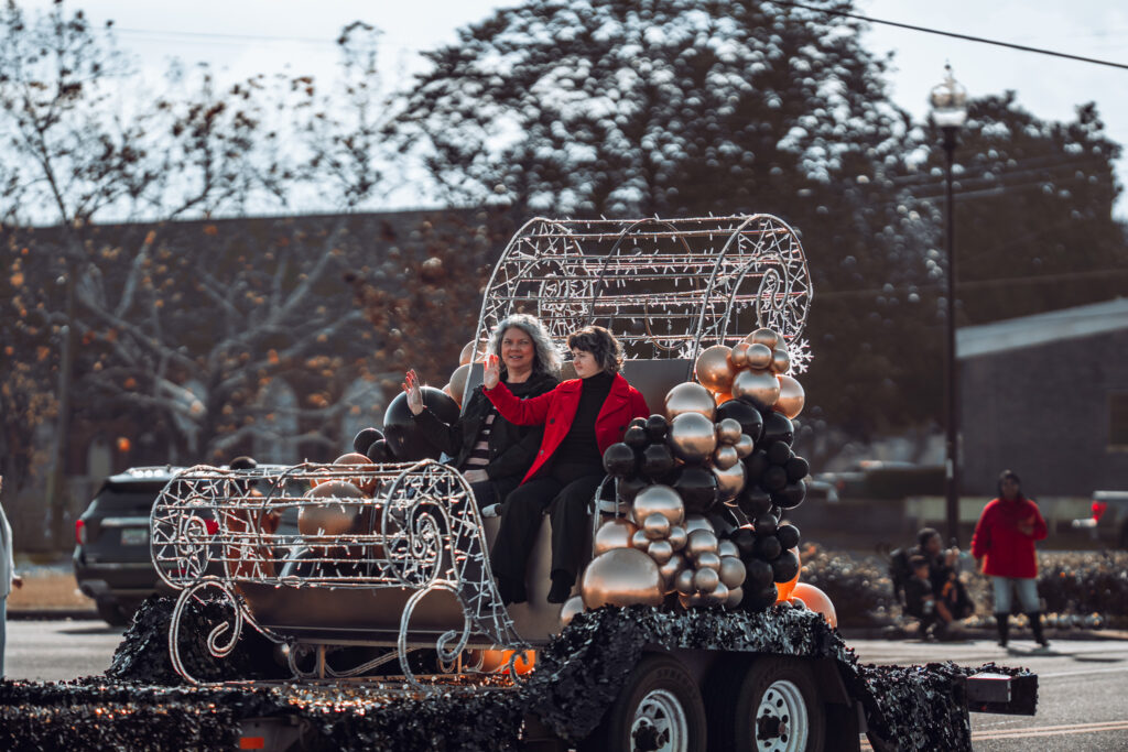 Two people riding a sleigh-themed parade float decorated with balloons