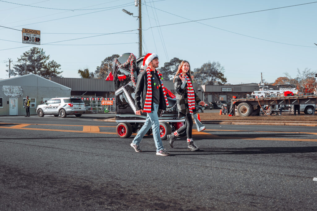 People in festive scarves and Santa hats walking in a holiday parade