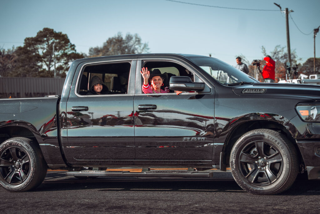 Smiling people wave from a black pickup truck during a parade