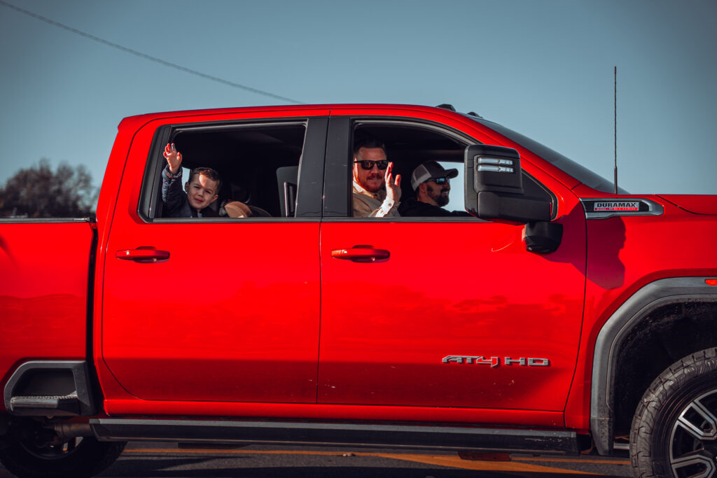 Smiling people waving from the windows of a bright red pickup truck