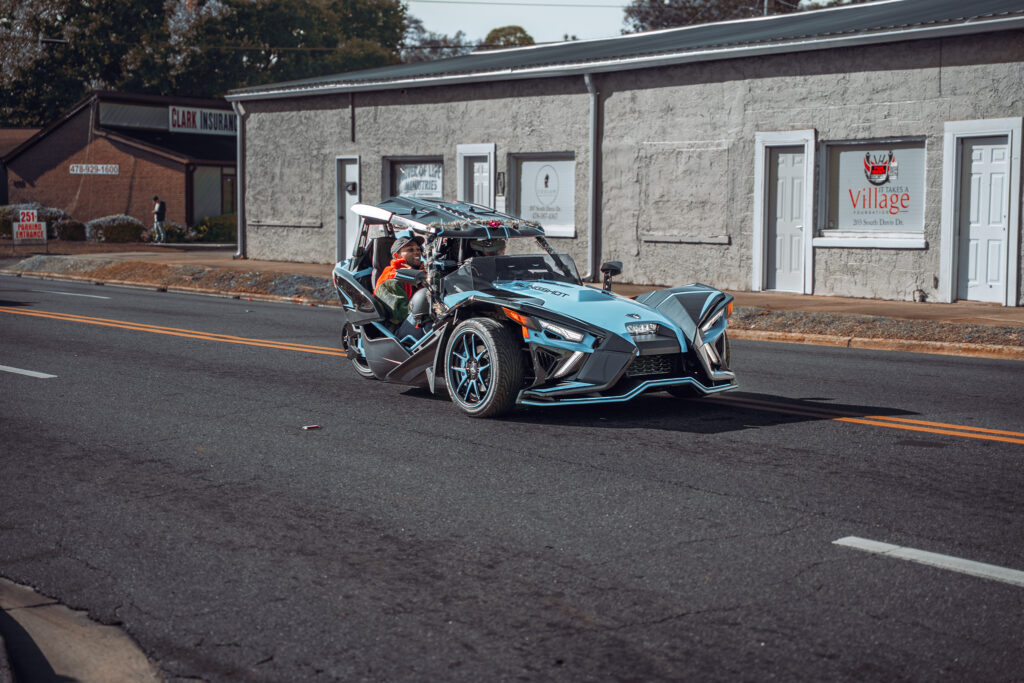 Polaris Slingshot three-wheeled roadster driving past older storefront buildings on a small-town main street