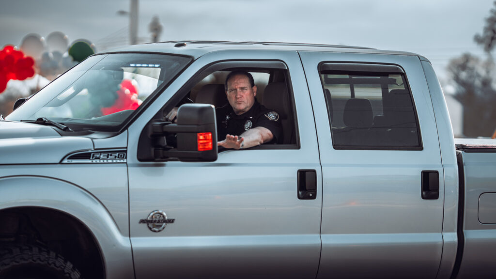 Uniformed police officer driving a silver pickup truck in a parade