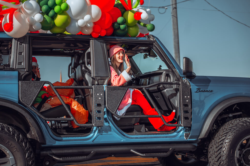 Smiling woman in red holiday outfit rides in balloon-decorated blue SUV